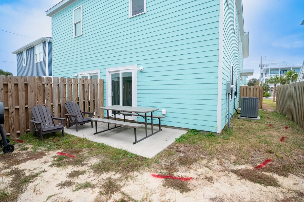 A cheerful exterior shot of the turquoise duplex homes, complete with a fenced yard, picnic table, and Adirondack chairs. The setup is perfect for large families, highlighting both privacy and shared outdoor spaces.
