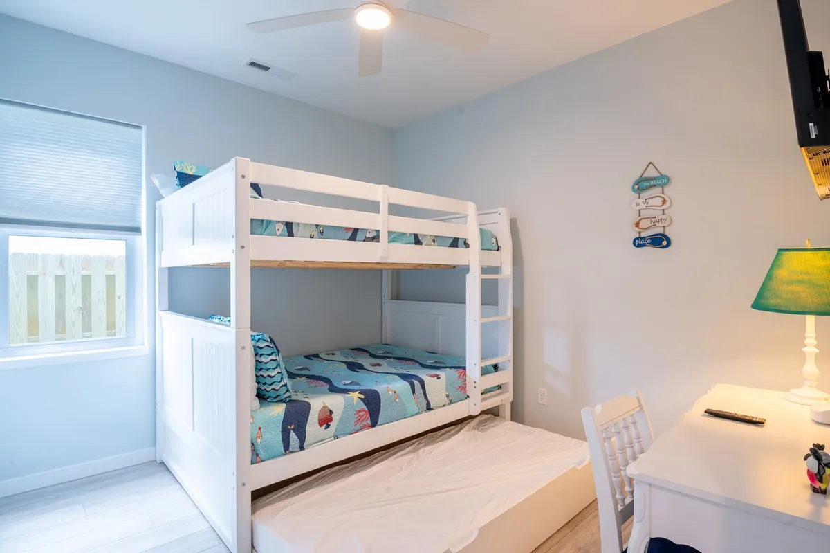 A cheerful bunk bedroom featuring a sturdy bunk bed with colorful bedding, a desk and chair ideal for study or creative play, decorative wall hangings, and a cozy lamp. The room is bright and inviting, perfect for children or teens who want both a place to rest and a spot to work or play.