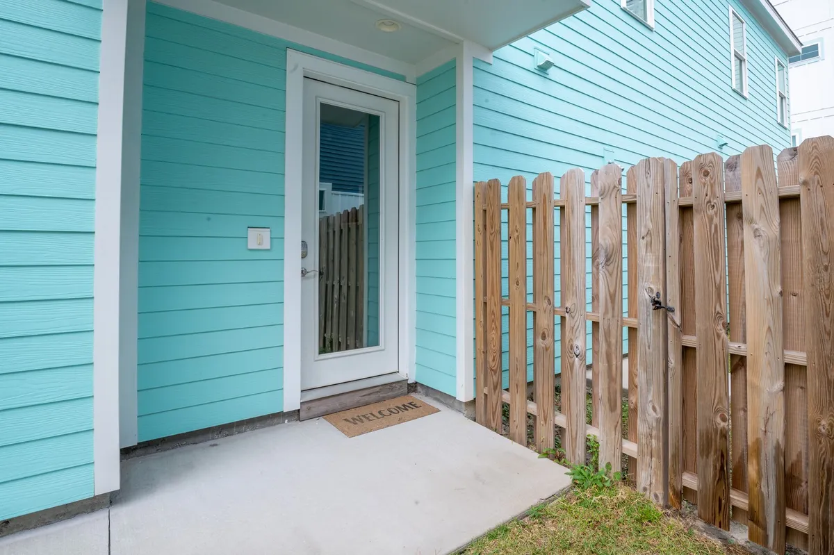 An exterior shot showing turquoise siding, a glass door, a wooden fence, and a welcome mat at the entry. This image represents the private driveways and entryways, emphasizing convenience and the unique setup of side-by-side duplex units.