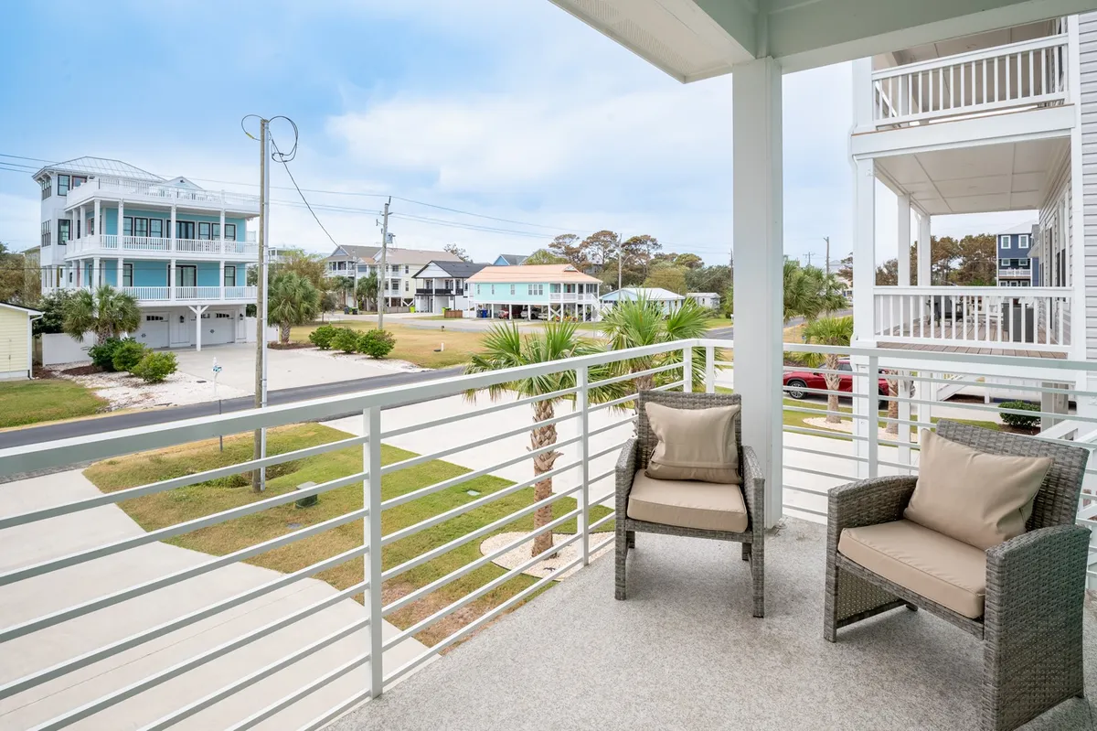 A tranquil exterior balcony with comfortable seating overlooks neighboring houses and swaying palm trees, creating a setting where guests can socialize, enjoy morning coffee, or relax after exploring the area. The view also subtly hints at the proximity to local attractions.