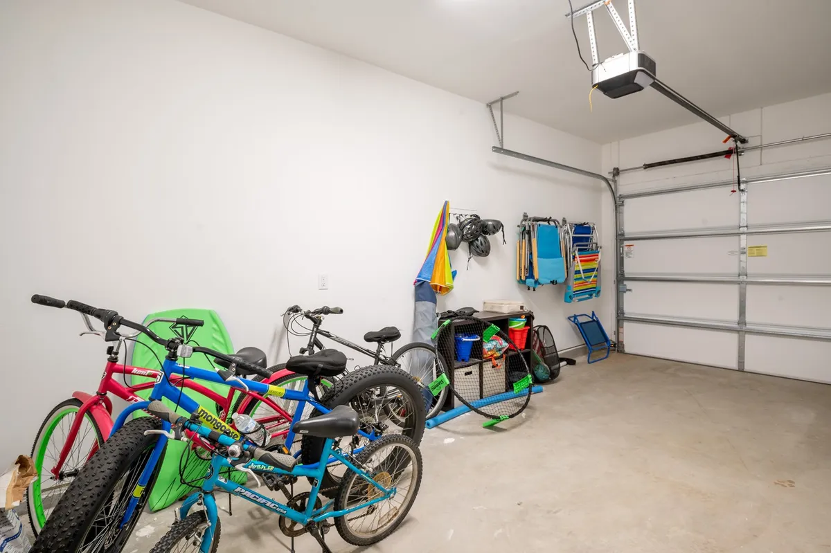 The image shows a garage or storage space filled with colorful bicycles and organized storage bins. Hanging towels add a casual, beachy vibe, and the overall mood is playful and active—suggesting preparations for family bike rides and easy access to outdoor adventures.