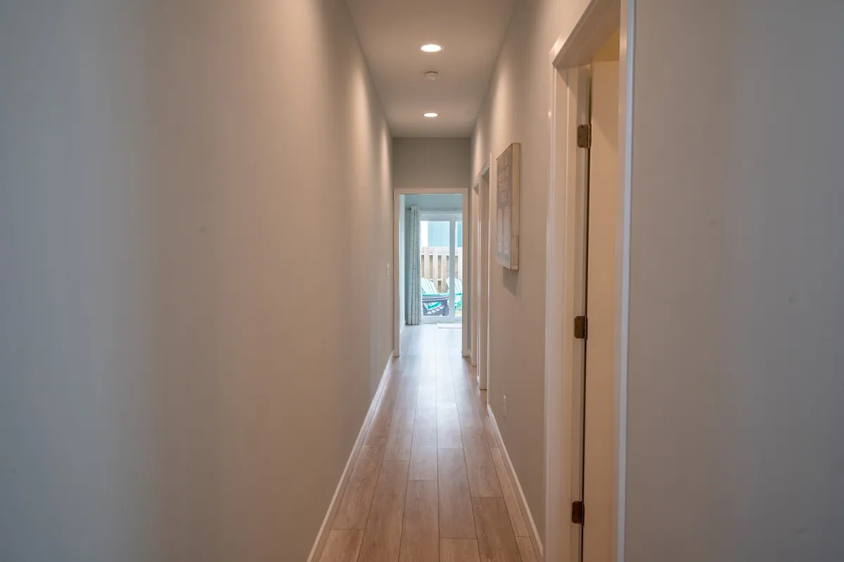 A long hallway with doors on either side and light streaming in from the end creates a welcoming, transitional space. The image suggests movement and anticipation, as if guests are gathering and preparing to step out together for a group activity or return home after a day of exploration.