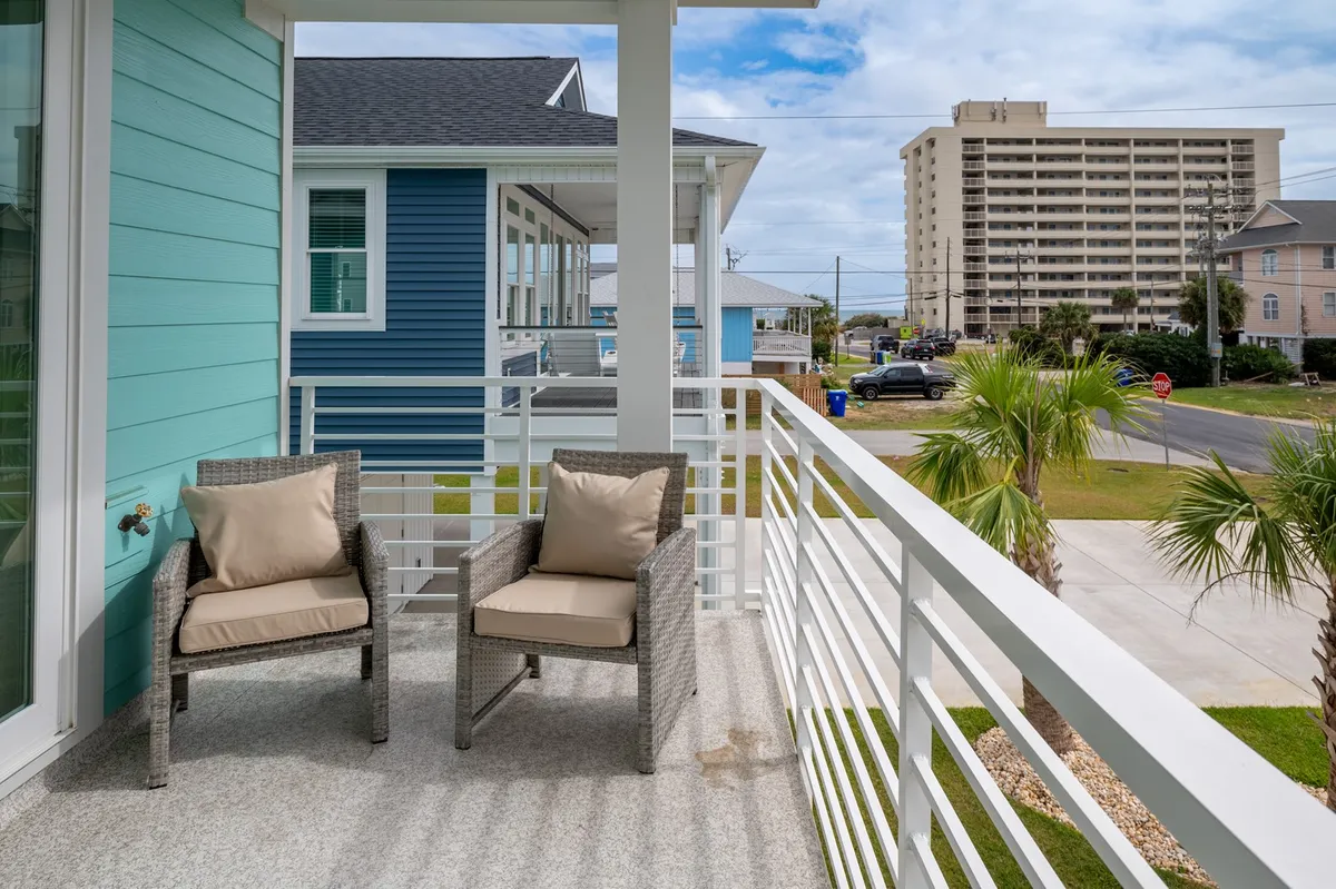 A tranquil porch setting with two wicker chairs and cushions set against a blue exterior wall, framed by palm trees. This breezy outdoor space suggests a perfect spot for al fresco dining or relaxing after a homemade meal.